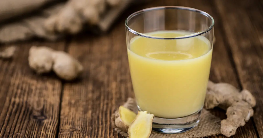 Glass of ginger juice on a rustic wooden table with fresh ginger root pieces nearby