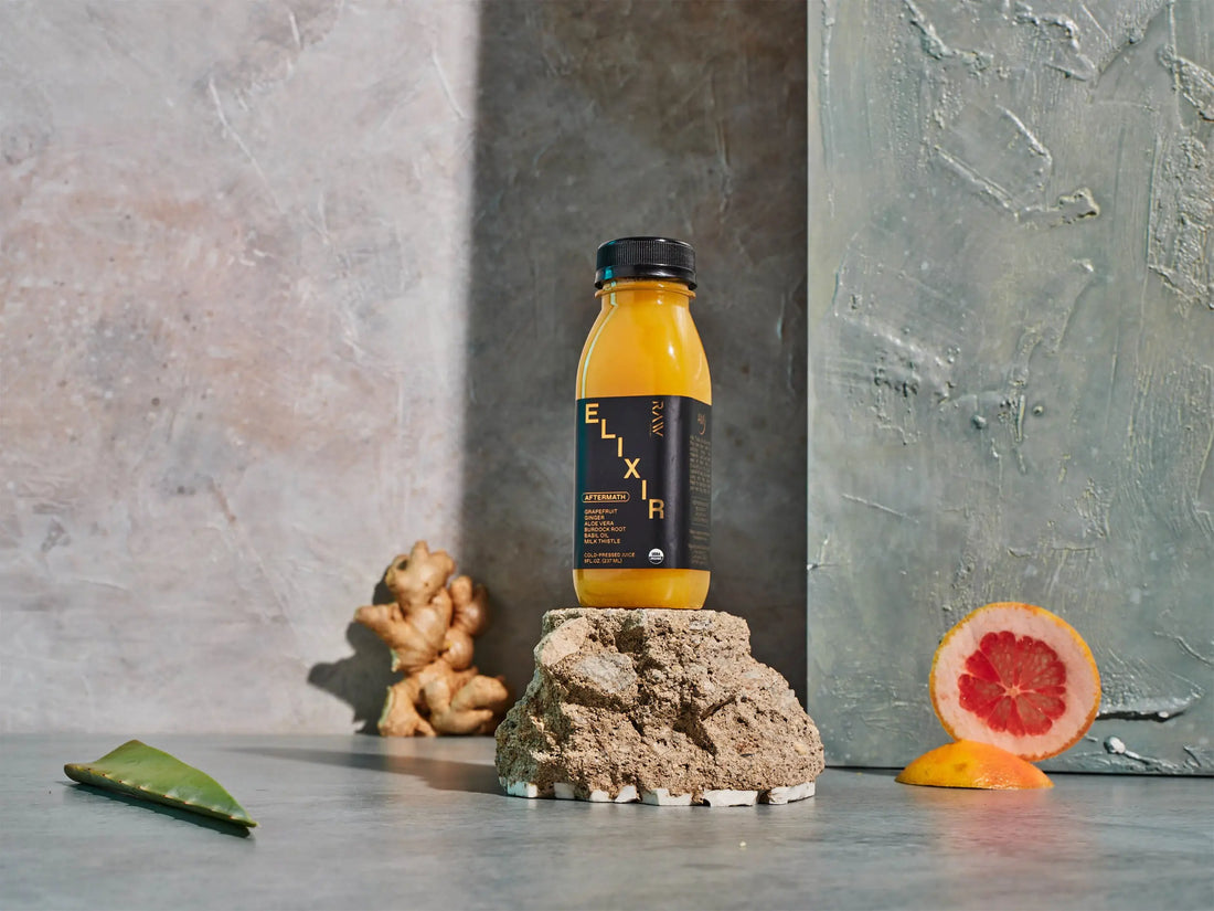 Best detox juice Elixir bottle displayed with fresh grapefruit, ginger, and aloe on stone backdrop
